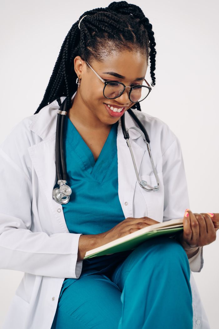 services-04 Smiling female doctor in scrubs with stethoscope reviewing patient notes indoors.