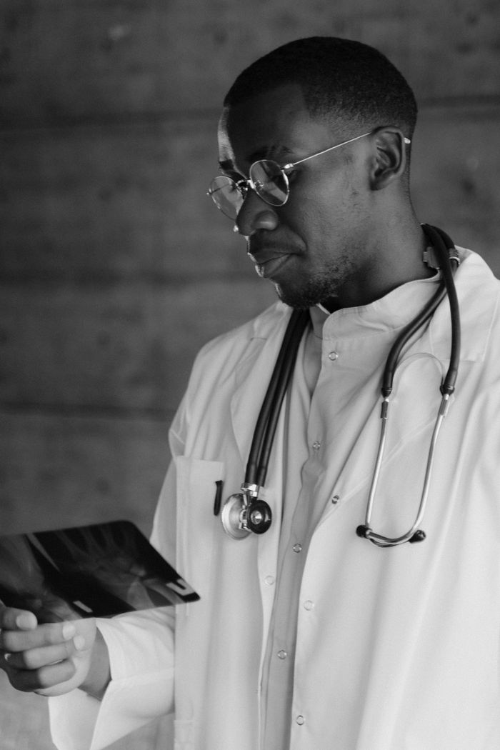 why-choose-us Monochrome image of a doctor examining an X-ray, wearing a stethoscope and lab coat.