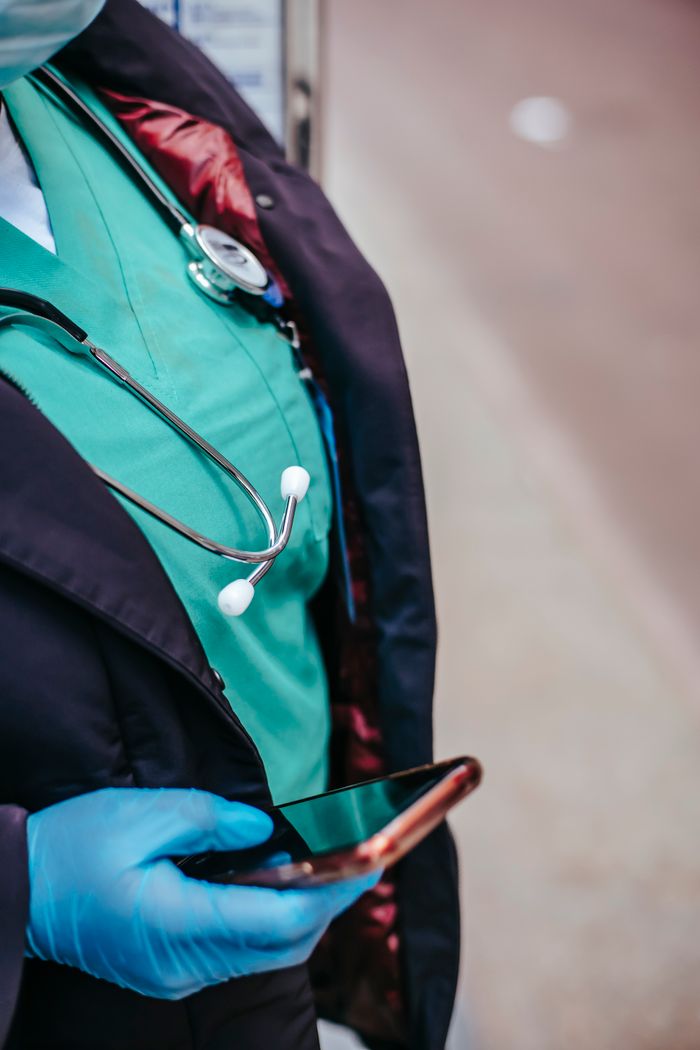 services-05 Crop anonymous female doctor in uniform with stethoscope touching black screen on cellphone in town