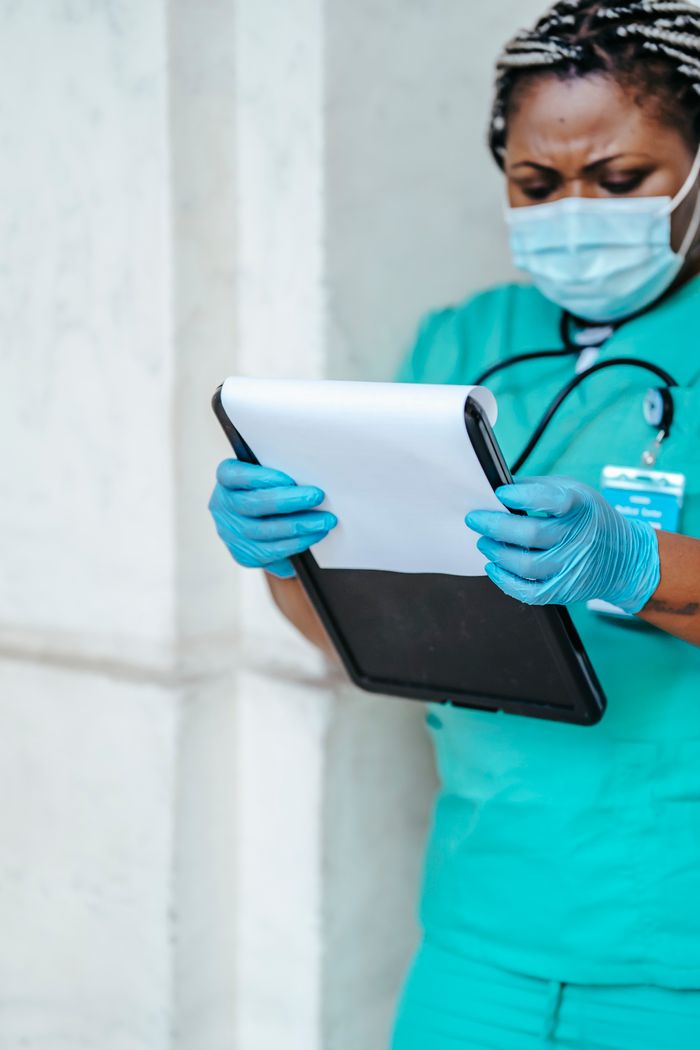 get-in-touch Crop African American female in uniform and gloves standing in hospital hallway and looking through papers