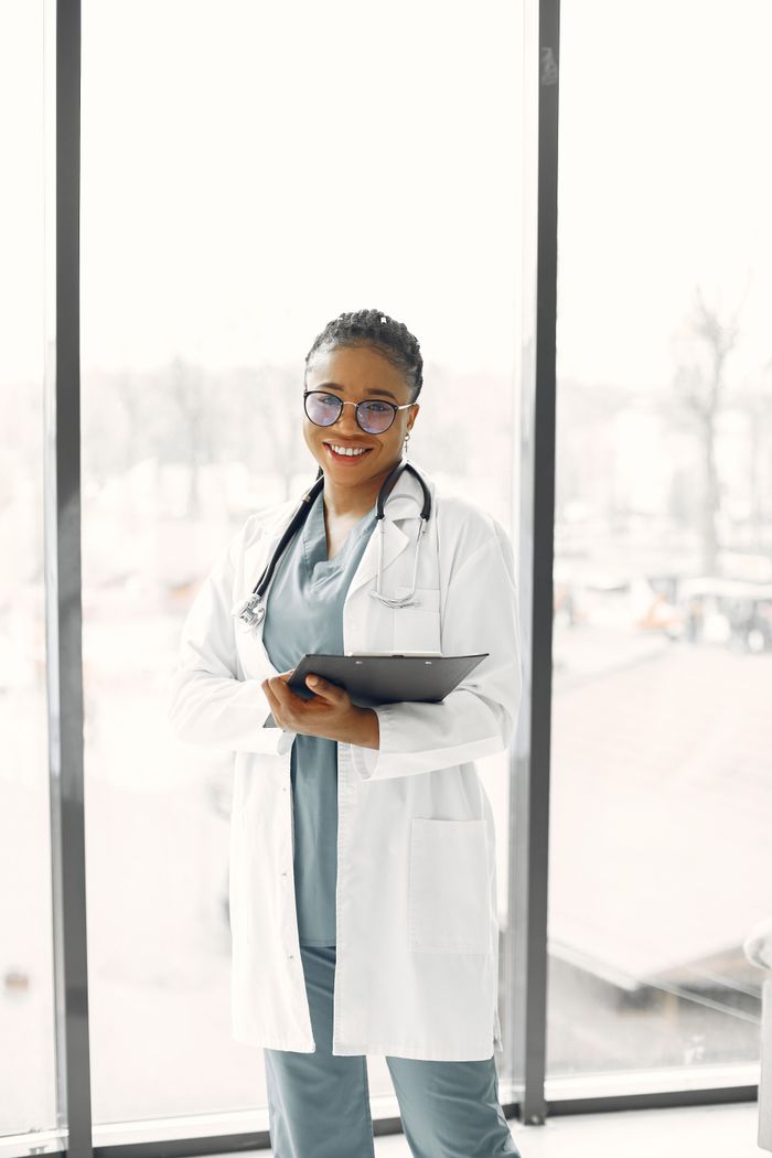 services-01 Smiling female healthcare professional with clipboard and stethoscope indoors.